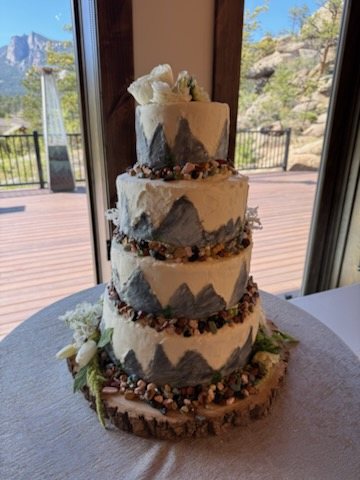Four-tier mountain-themed wedding cake with a Rocky Mountain view behind it